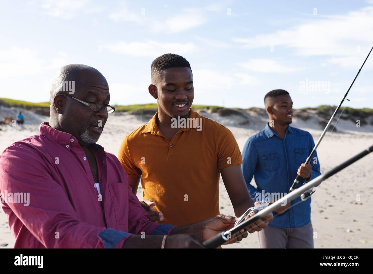 Padre afroamericano che insegna a suo figlio come usare la pesca canne sulla spiaggia Foto Stock