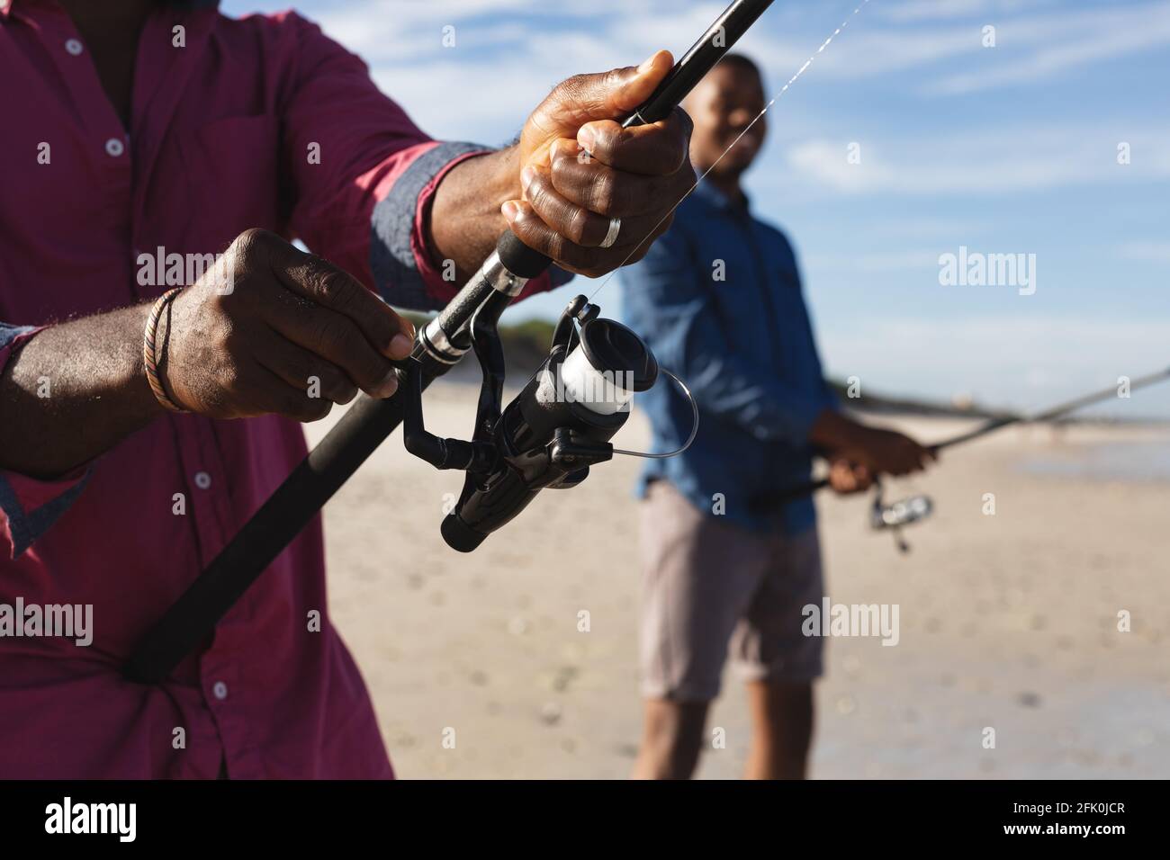 Metà sezione del padre afroamericano e suo figlio con pesca canne pesca insieme in spiaggia Foto Stock