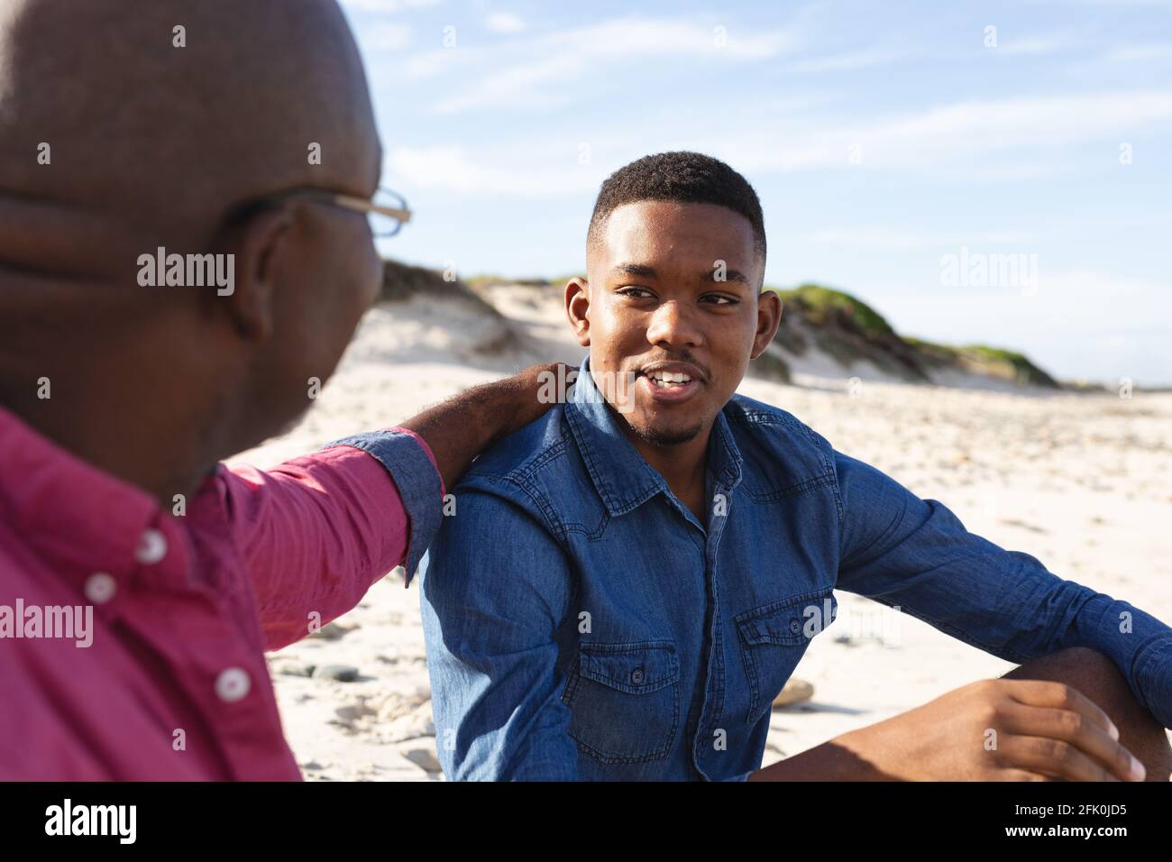 Padre afroamericano che parla con suo figlio mentre sedeva a. la spiaggia Foto Stock