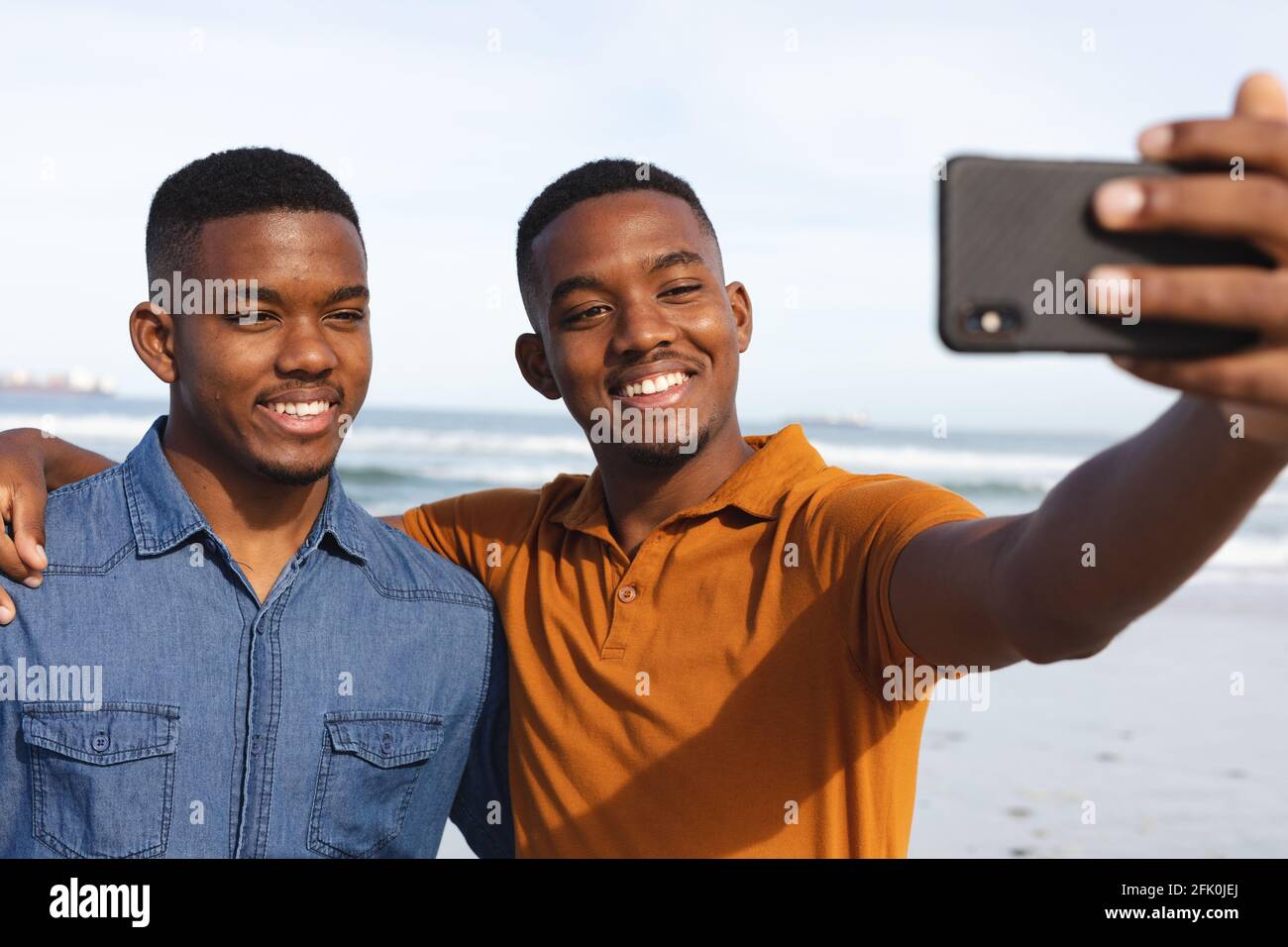 I fratelli afro-americani sorridono mentre prendono un selfie dallo smartphone in spiaggia Foto Stock