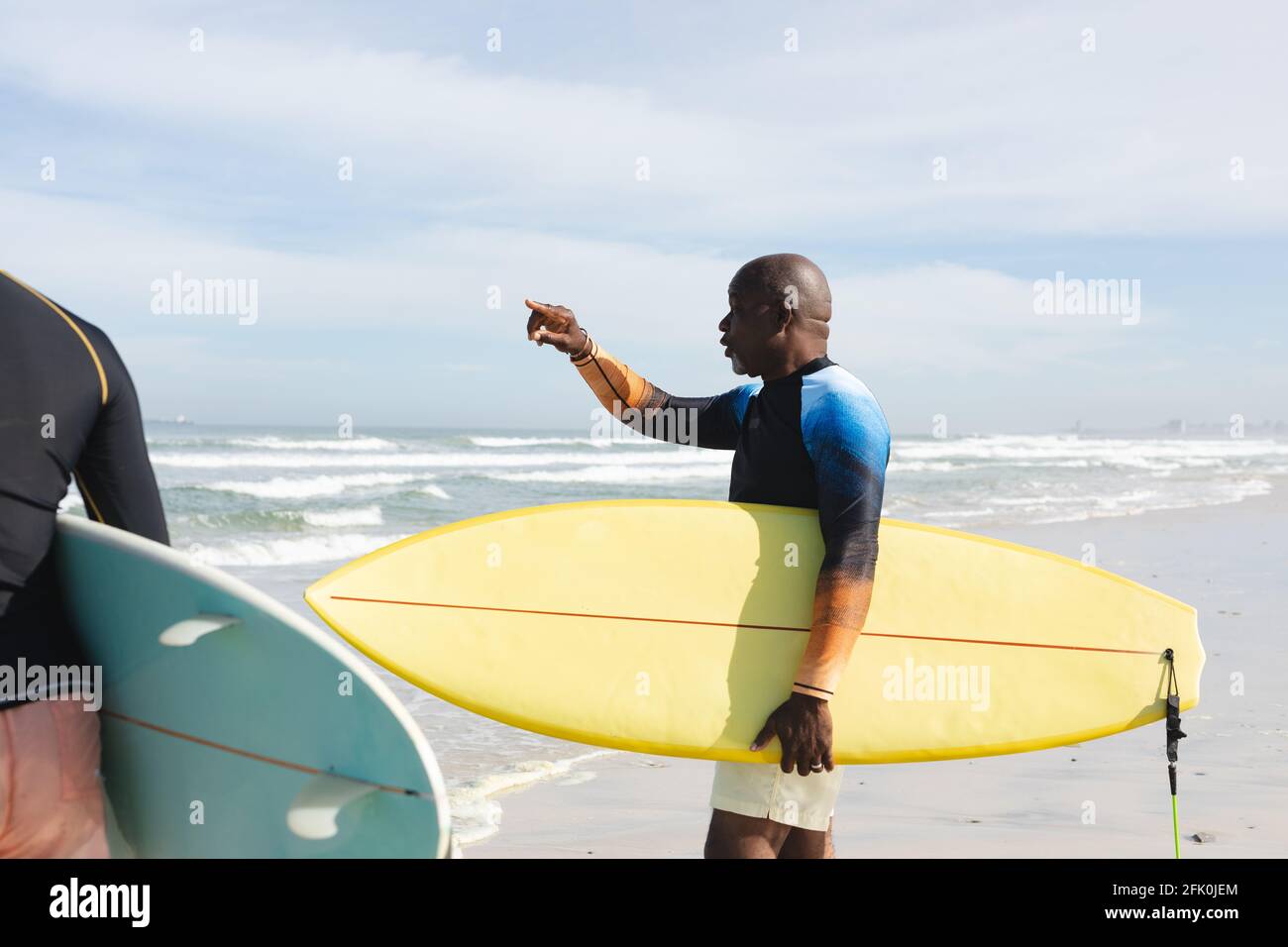 Uomo anziano afroamericano con tavola da surf che punta verso le onde in spiaggia Foto Stock