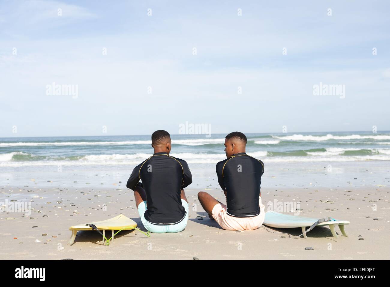 Vista posteriore dei fratelli afroamericani con tavole da surf sedute a. la spiaggia Foto Stock