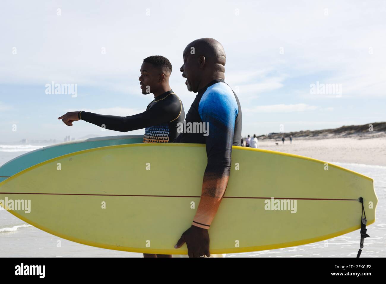 Padre e figlio afro-americano con tavole da surf che camminano verso il onde in spiaggia Foto Stock