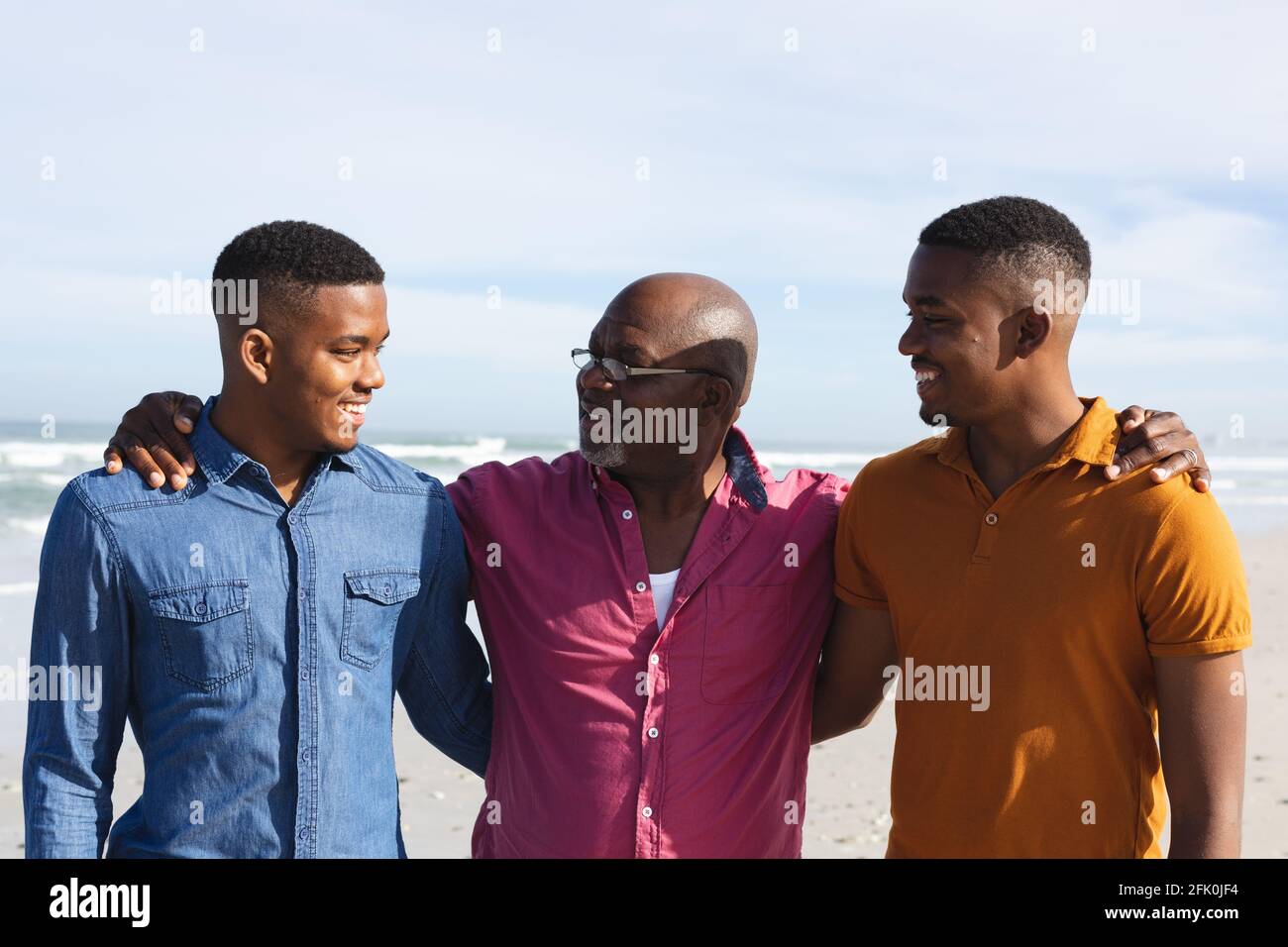 Il padre afroamericano e i suoi due figli sorridono mentre si levano in piedi in spiaggia Foto Stock