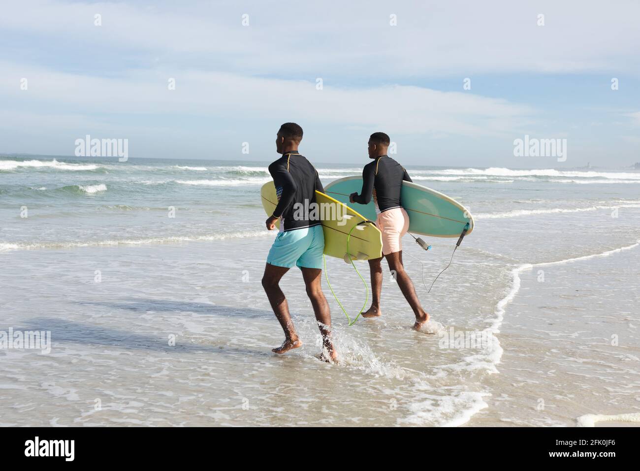 Fratelli afroamericani con tavole da surf che corrono verso le onde a. la spiaggia Foto Stock