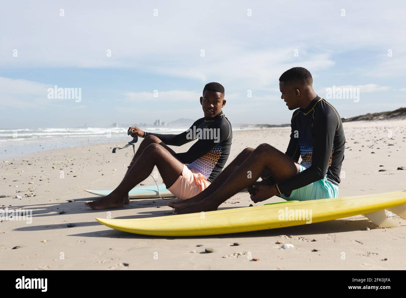 Fratelli afroamericani con tavole da surf seduti in spiaggia Foto Stock