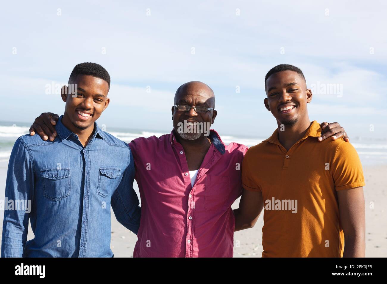 Ritratto del padre afroamericano e dei suoi due figli sorridenti mentre si sta in piedi insieme in spiaggia Foto Stock