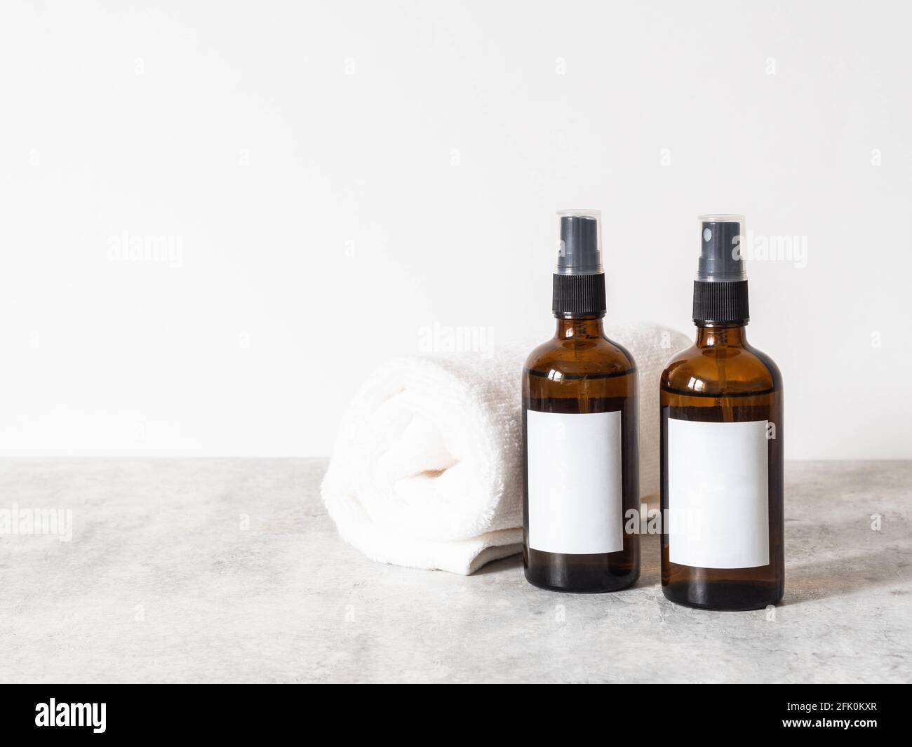 Due bottiglie di vetro marrone con etichetta bianca e asciugamano bianco su tavolo grigio in bagno. Vista frontale. Spazio di copia. Blogging concetto minimo di bellezza, cosmetici Foto Stock