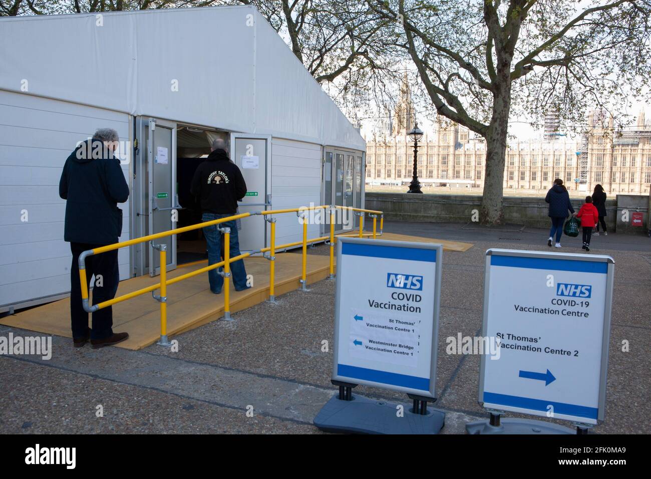 Londra, Regno Unito, 27 aprile 2021: La gente si accoda alla fine di un centro di vaccinazione nei terreni del St Thomas's Hospital, di fronte al Parlamento sulla riva opposta del Tamigi. Il primo ministro Boris Johnson si trova ancora di fronte alle accuse di aver preferito che "i corpi si accumulino" piuttosto che avere un terzo blocco. Anna Watson/Alamy Live News Foto Stock