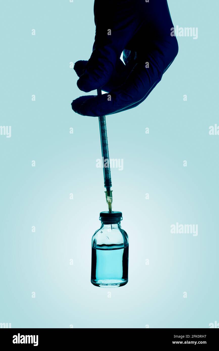 chiusura di un operatore sanitario o di laboratorio, indossando guanti chirurgici, riempiendo una siringa da un flaconcino con un liquido blu Foto Stock