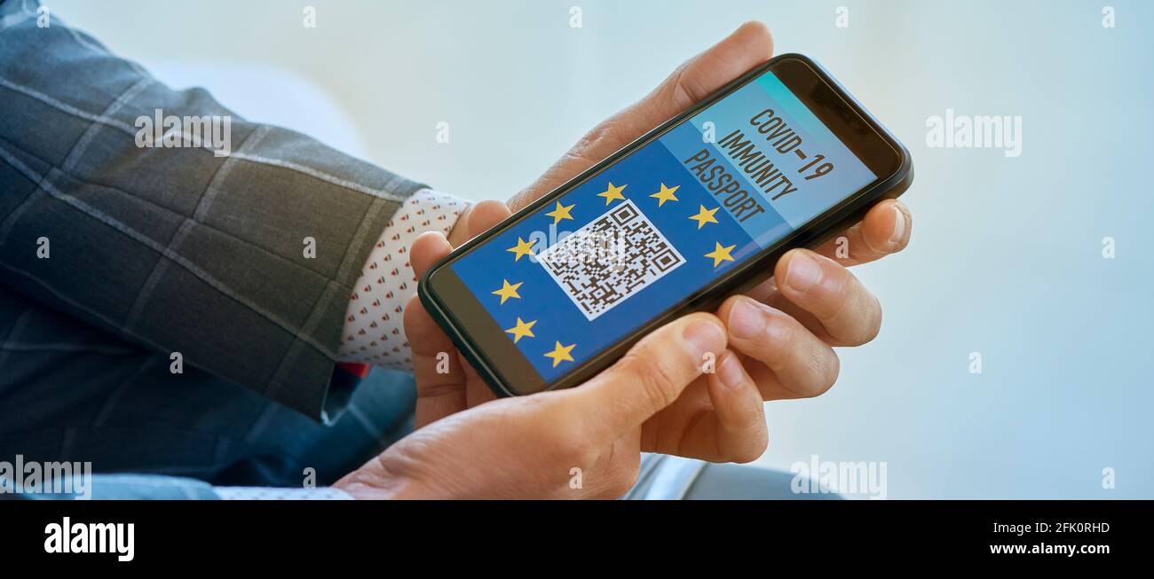 Un uomo d'affari, nella sala d'attesa di un aeroporto, ha un mock elettronico europeo covid-19 passaporto di immunità con un codice QR nel suo smartphone, in una PAN Foto Stock