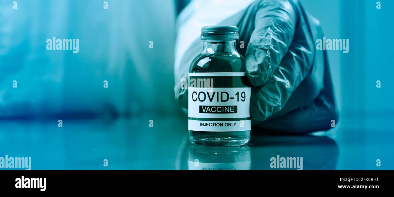 chiusura di un operatore sanitario o di laboratorio, indossando guanti chirurgici, mostrante una fiala simulata di un vaccino covid-19, in un formato panoramico da utilizzare come Foto Stock