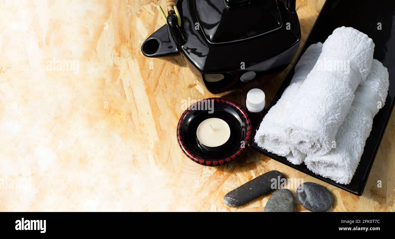Teiera in ceramica nera in stile orientale lampada aroma e rotoli di olio aromatico di asciugamani bianchi su un piatto di ceramica e ciottoli di mare per il massaggio viso. Foto Stock