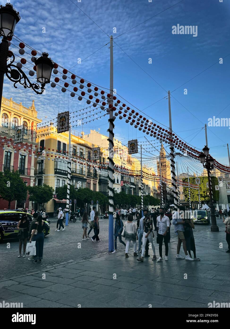 SEVILLA, SPAGNA - Apr 18, 2021: Gruppo di persone che camminano in Plaza San Francisco a Siviglia con l'illuminazione della fiera di aprile con la Giralda nel b Foto Stock