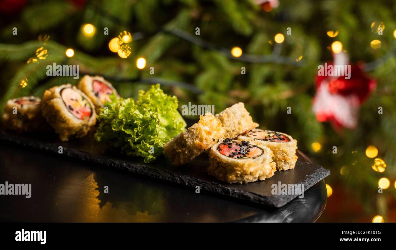 Rotolo di sushi personalizzato in tempura con nori, salmone fresco, tonno, avocado, caviale di masago, condito con salsa di ananas e insalata da versare come decorazione Foto Stock