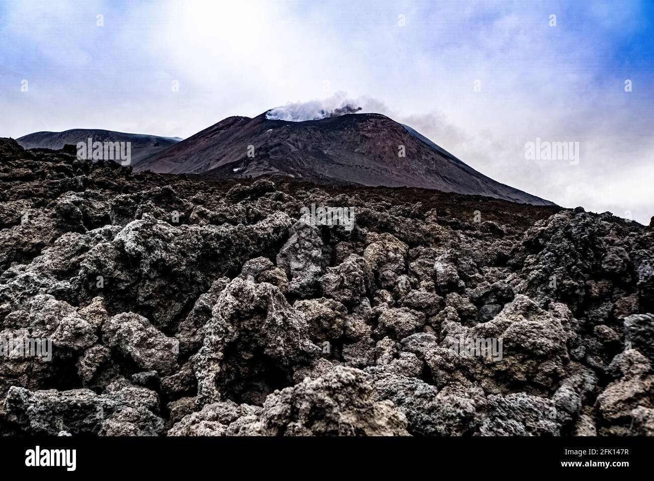 L'Etna sputa cenere e fumo. Roccia lavica in primo piano Foto Stock