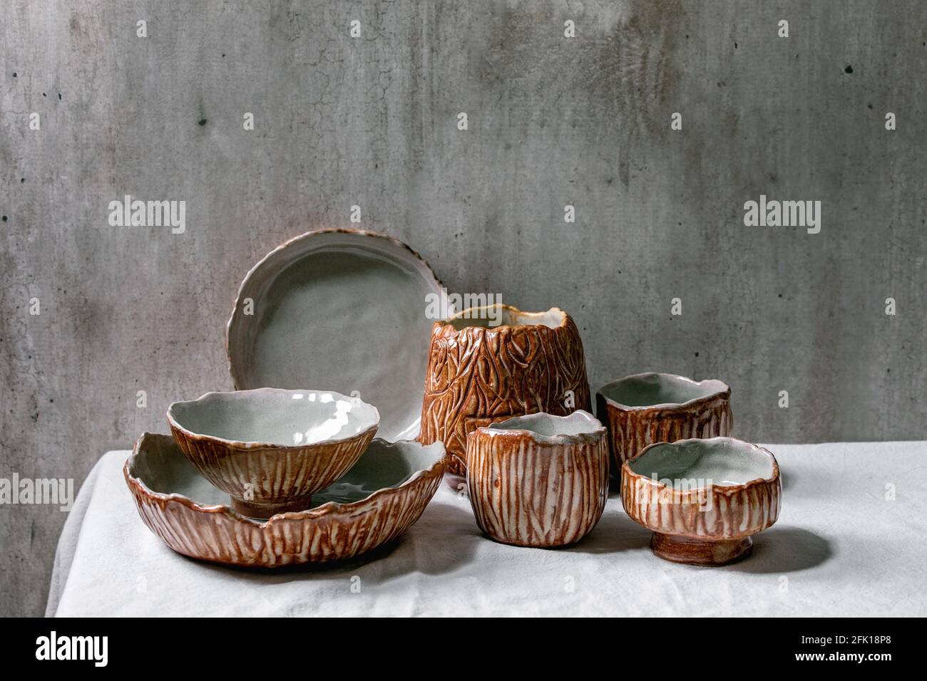 Set di ciotole vuote artigianali in ceramica coprite da una texture grigia e marrone smalto su tovaglia di lino bianco con parete grigia dietro. Spazio di copia. Foto Stock
