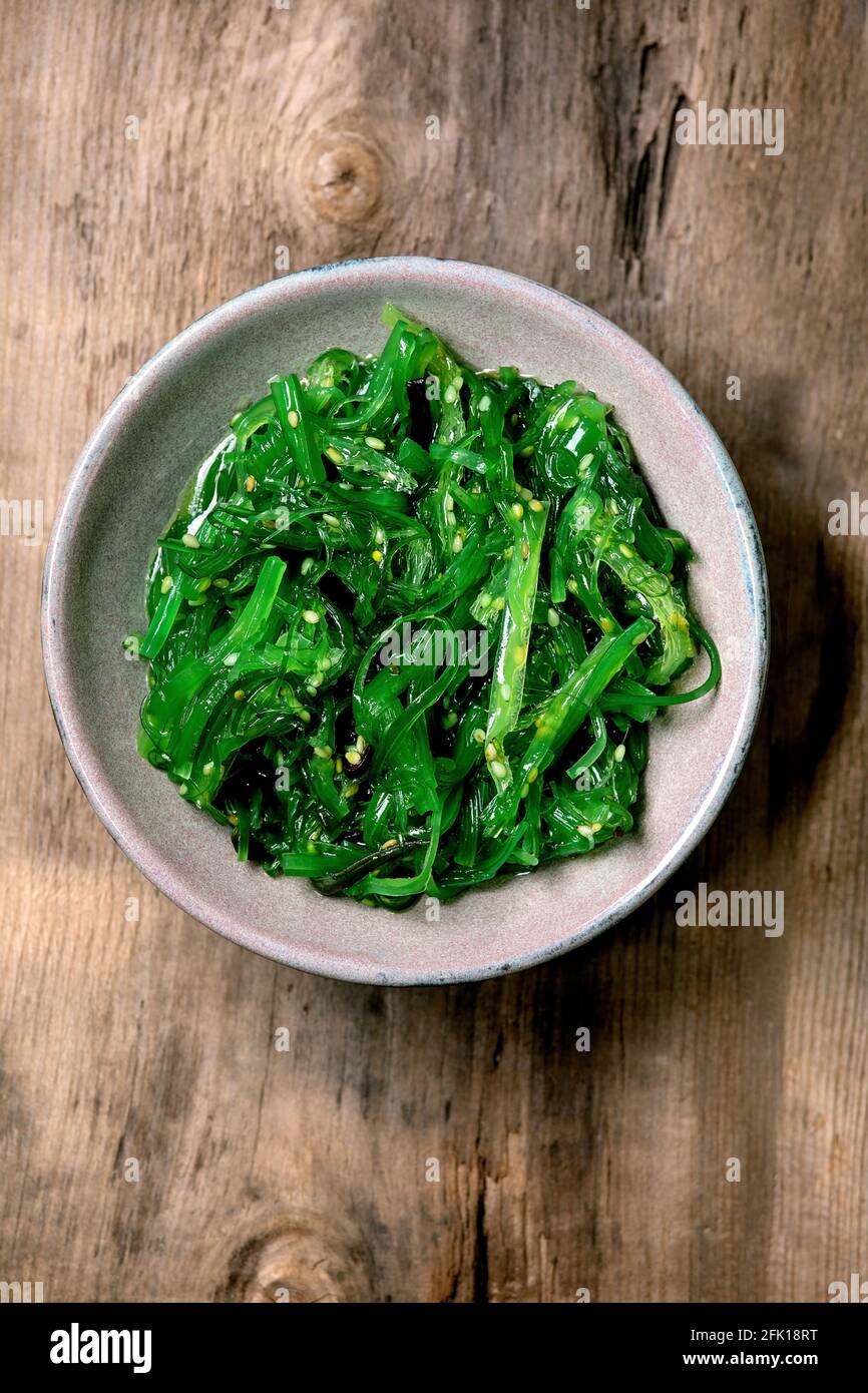 Insalata giapponese di alghe Wakame chuka con semi di sesamo in piastra di ceramica su vecchio sfondo di legno. Disposizione piatta, spazio di copia Foto Stock