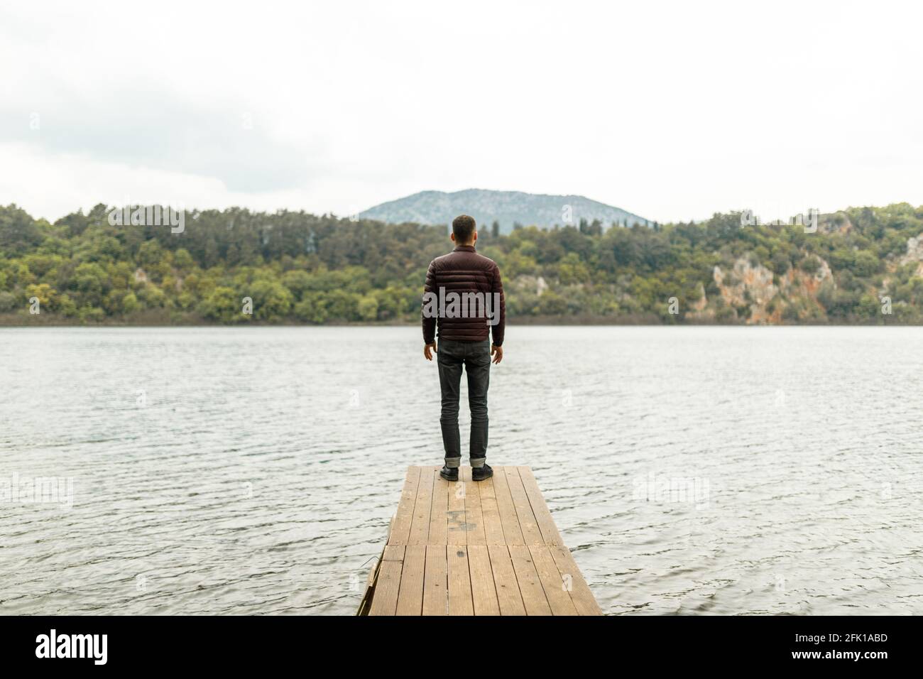 Uomo in piedi solo su un molo di legno vicino al lago con vista sulla natura Foto Stock