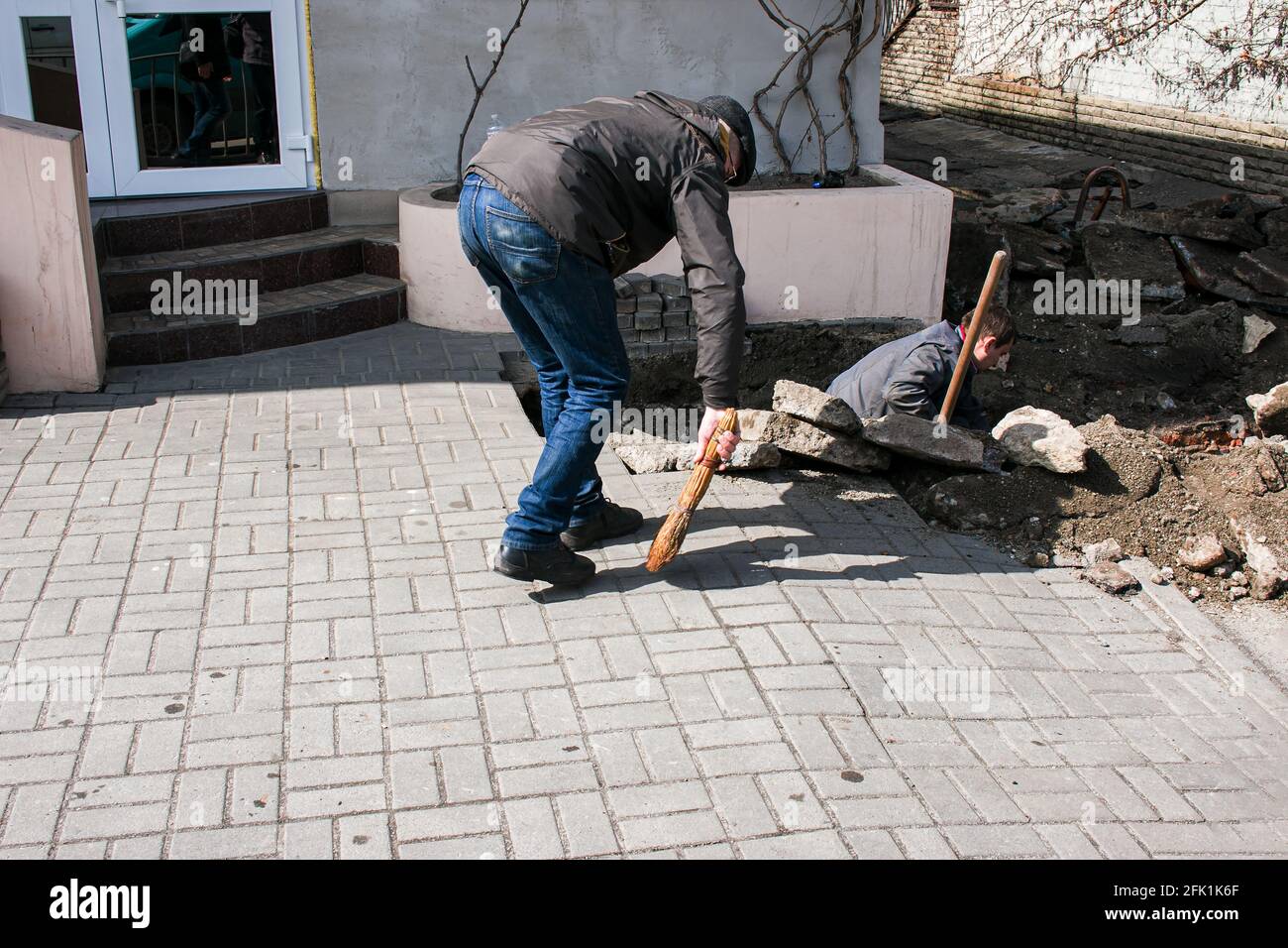 Dnepropetrovsk, Ucraina - 03.26.2021: Un lavoratore spazza su sporcizia dopo la sostituzione dei tubi fognari. Foto Stock