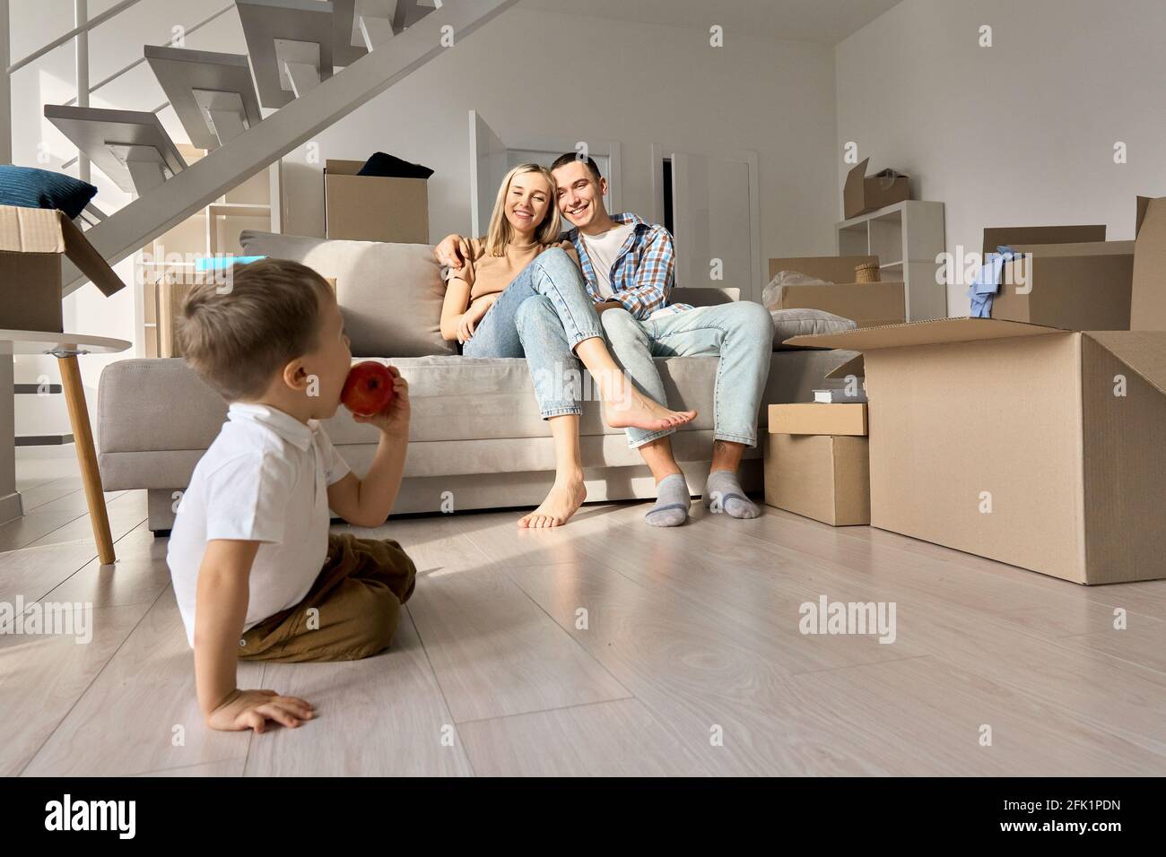 Felice coppia di famiglia con figlio di bambino che si rilassa durante il giorno in movimento in un nuovo salotto di casa. Foto Stock