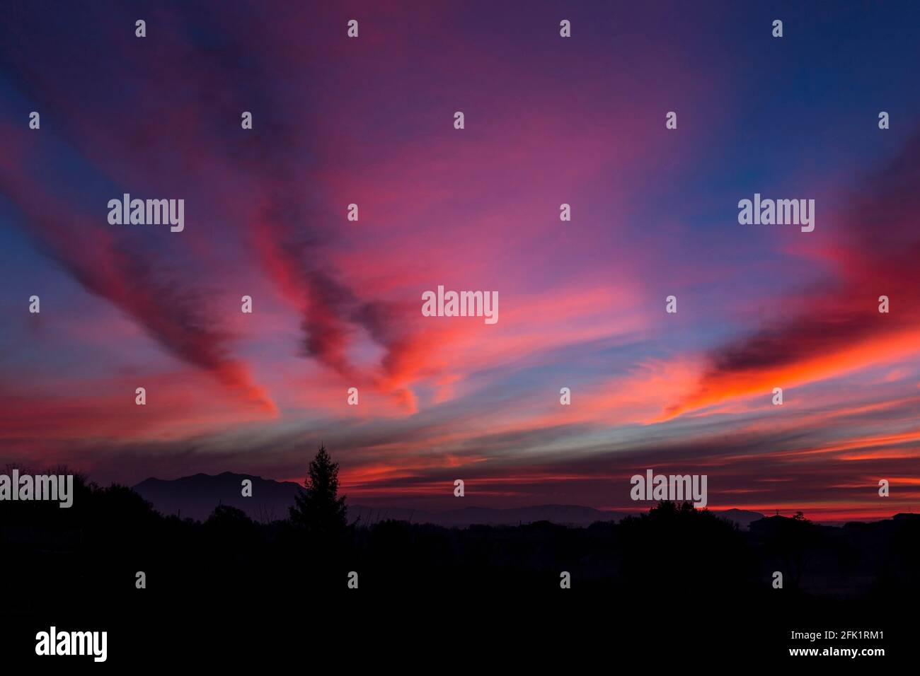 I colori intensi dell'alba. Le nuvole colorate attraversano il cielo come linee fiammeggianti sopra il profilo scuro del Monte Soratte, nella campagna romana. Foto Stock