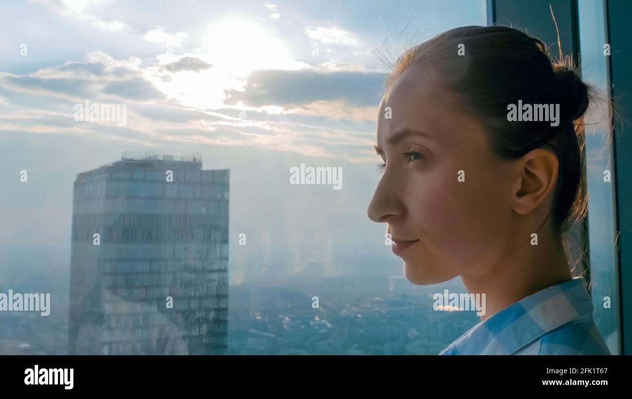 Donna che guarda il paesaggio urbano attraverso la finestra del grattacielo - lato visualizza Foto Stock
