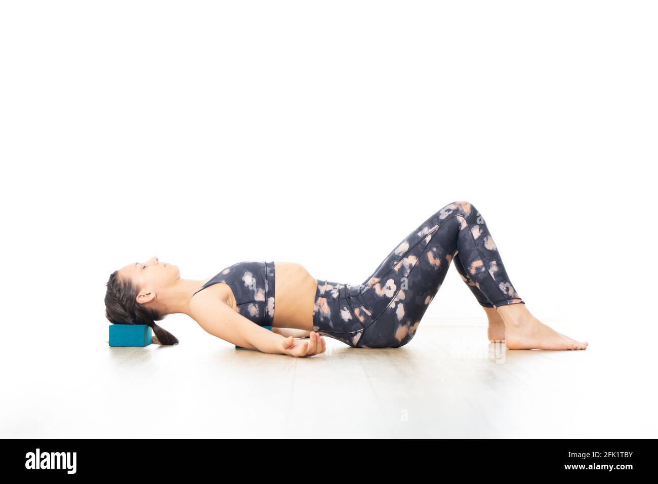 Giovane donna sportiva attraente in luminoso studio di yoga bianco, stretching e relax durante il restorative yoga utilizzando gadget. Uno stile di vita sano e attivo Foto Stock