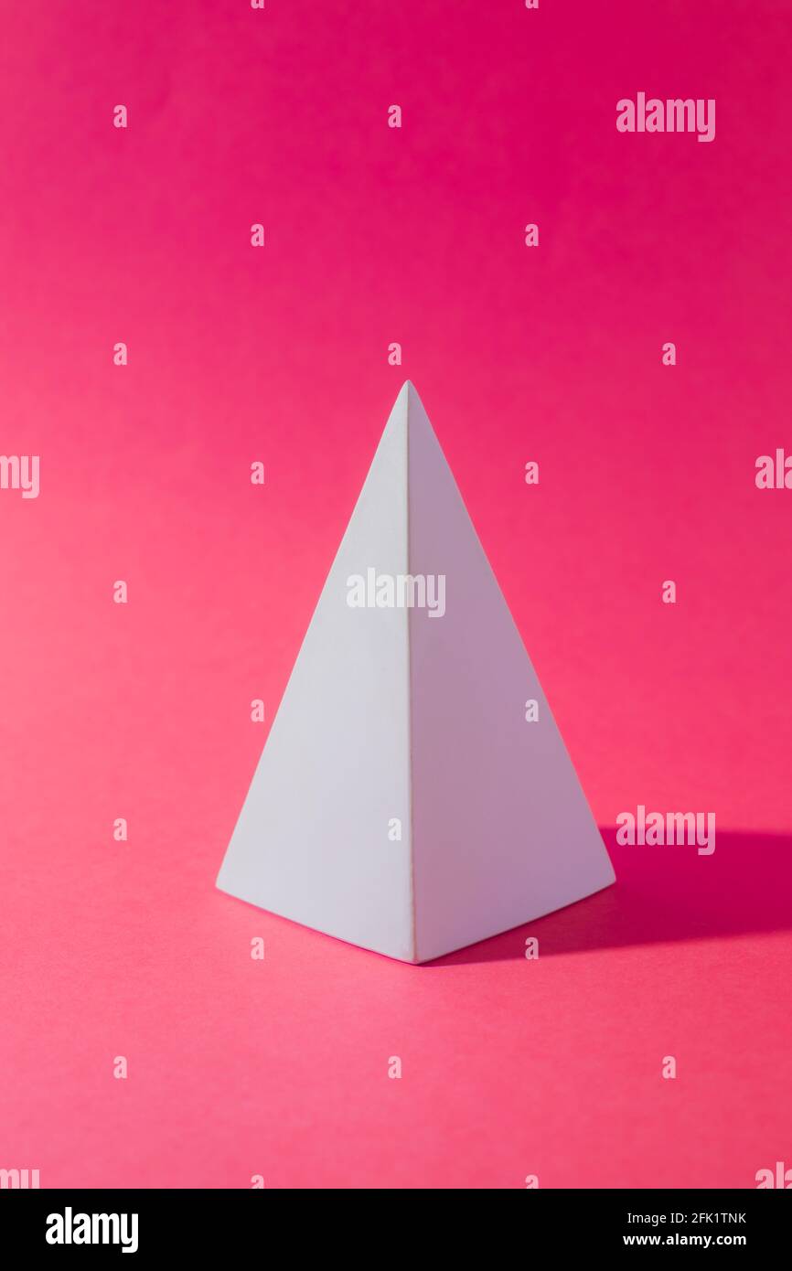 Forma geometrica astratta della piramide bianca sul rosa Foto Stock