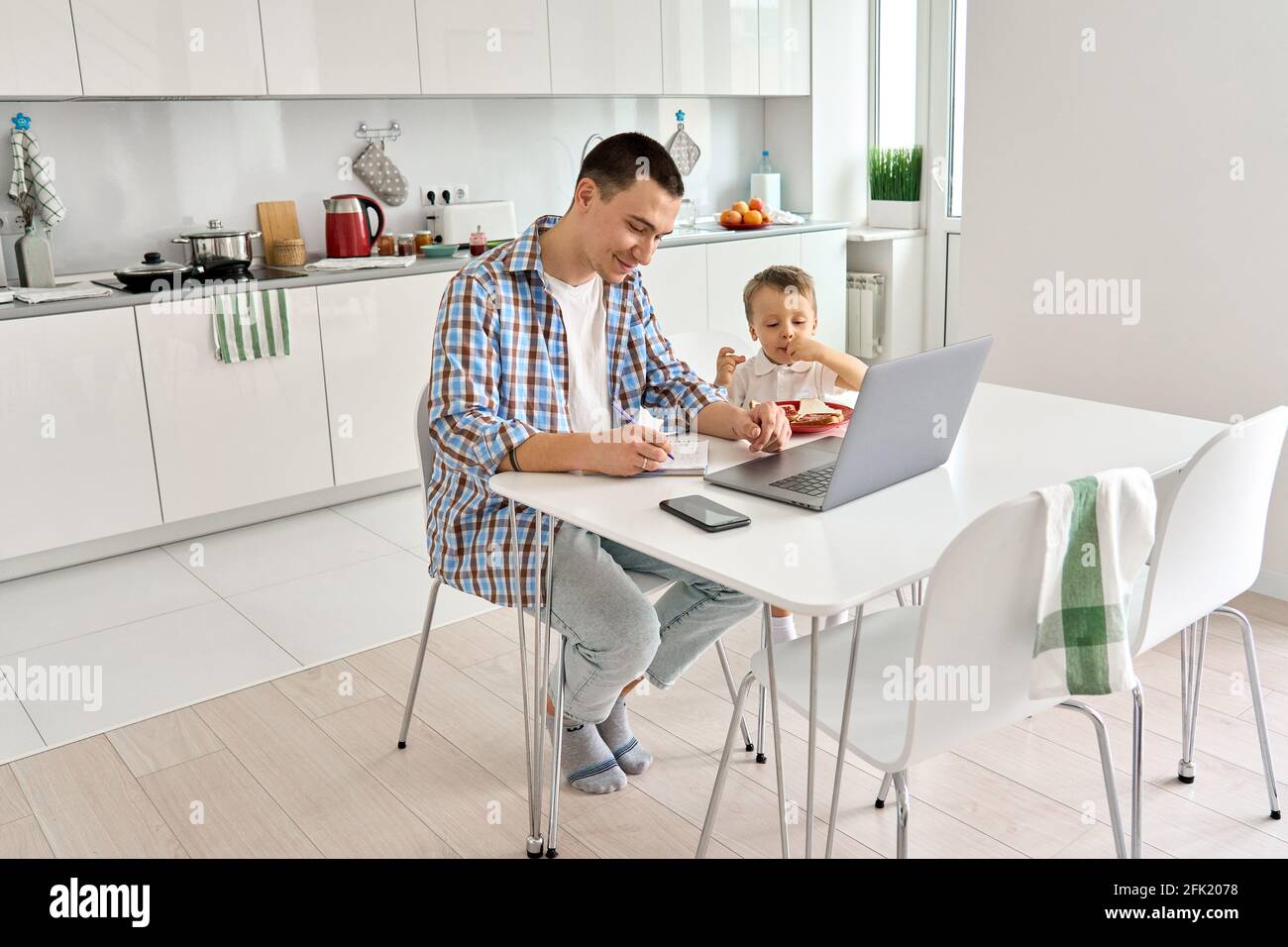 Giovane papà seduto in cucina a casa con bambini guarda corsi di formazione sul pc. Foto Stock