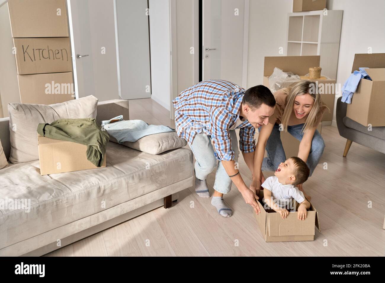 Felici genitori che spingono scatola di cartone con il bambino in nuovi appartamenti ipotecari. Foto Stock