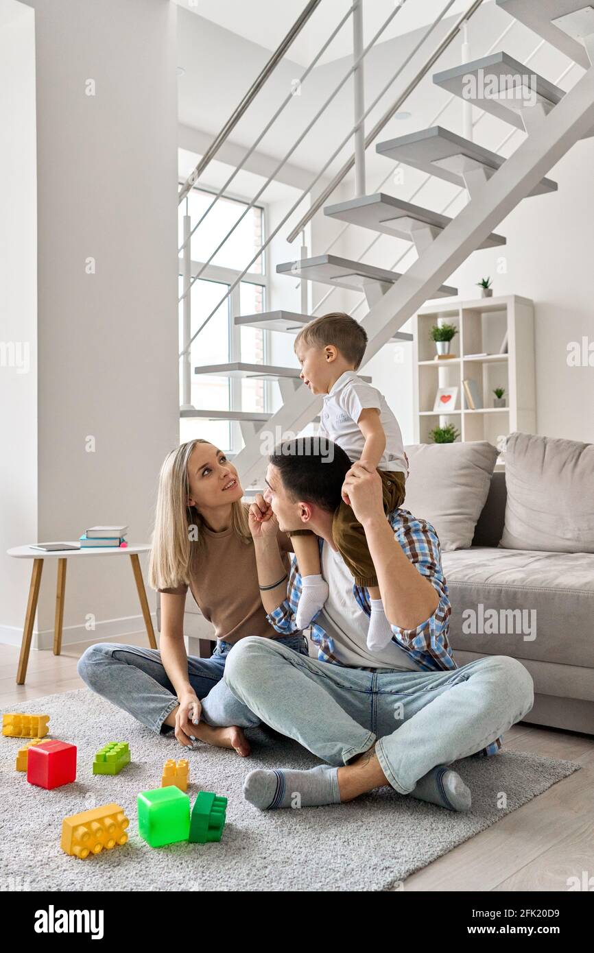Giovane famiglia con ragazzo sul collo del papà seduto sul pavimento in un moderno soggiorno. Foto Stock
