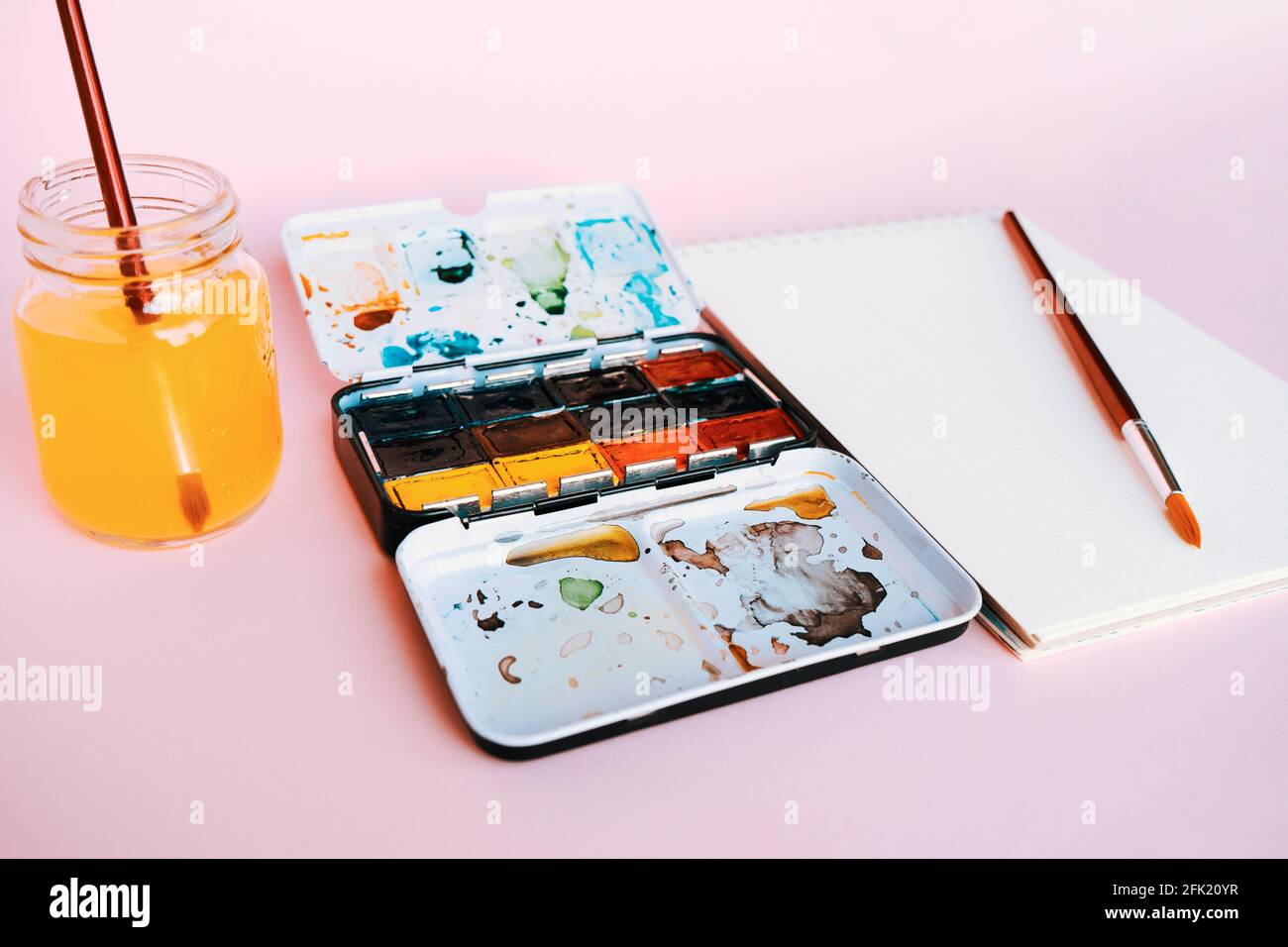 Taccuino bianco di colore dell'acqua, l'arte fornisce i pennelli, le vernici, i acquerelli e la tazza di acqua. Studio d'arte. Lezioni di disegno. Foto Stock