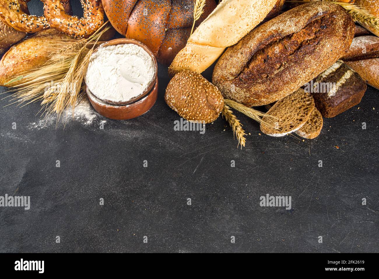Assortimento di vari deliziosi pane appena sfornato, su fondo nero cemento vista dall'alto spazio copia Foto Stock