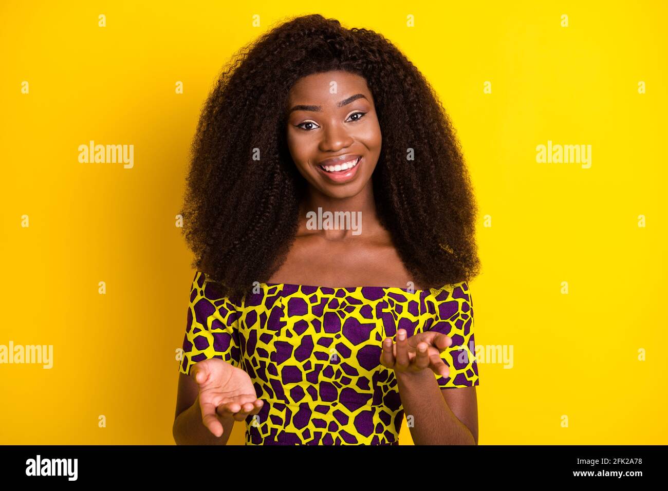 Ritratto di bella ragazza con capelli ondulati allegra che ti dice di condividere le notizie isolato su sfondo giallo brillante Foto Stock