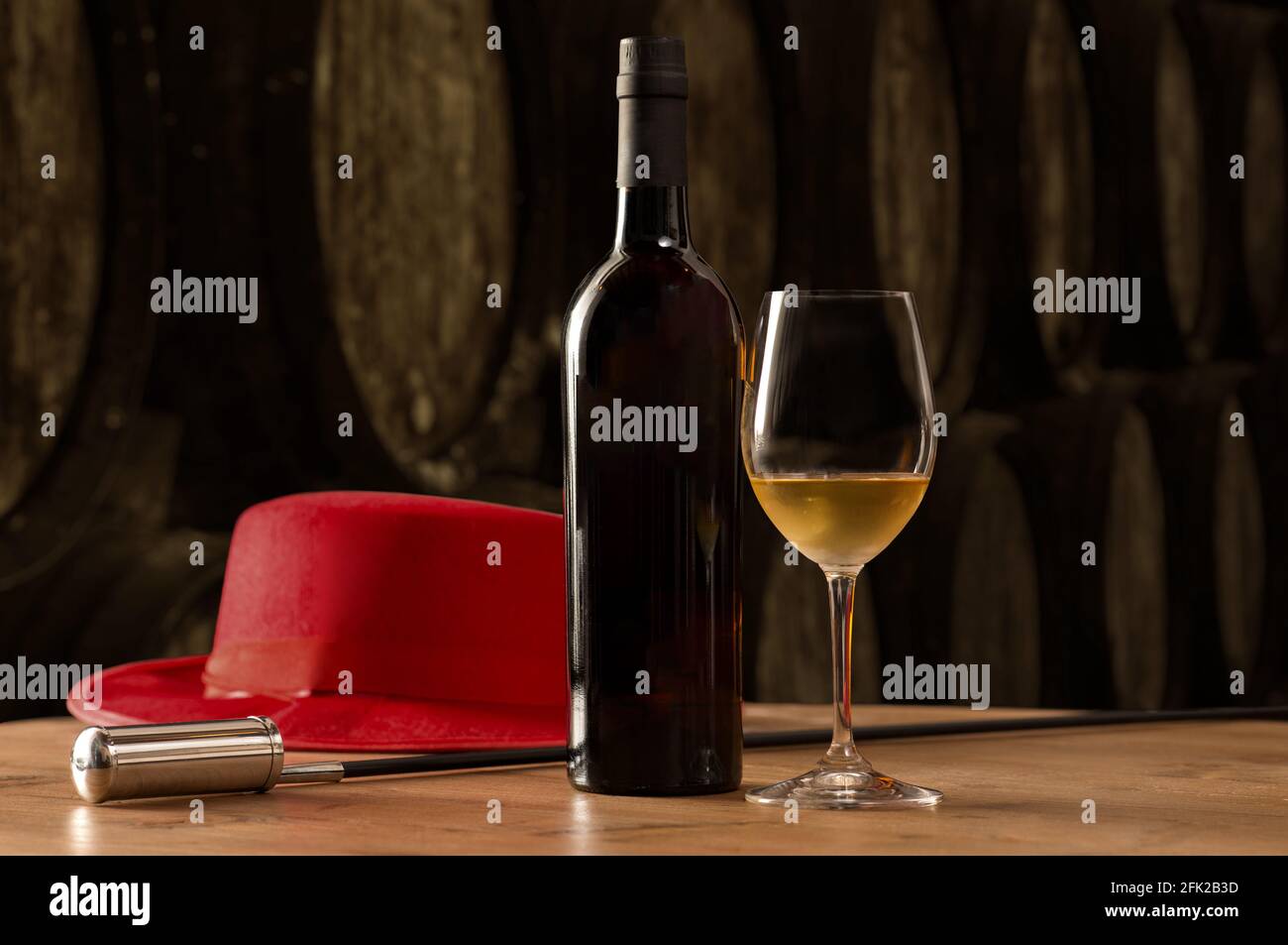 Bottiglia e bicchiere di vino fino bianco sherry in cantina con tipico cappello rosso andaluso e distributore di vino sul tavolo sullo sfondo della vecchia barra Foto Stock