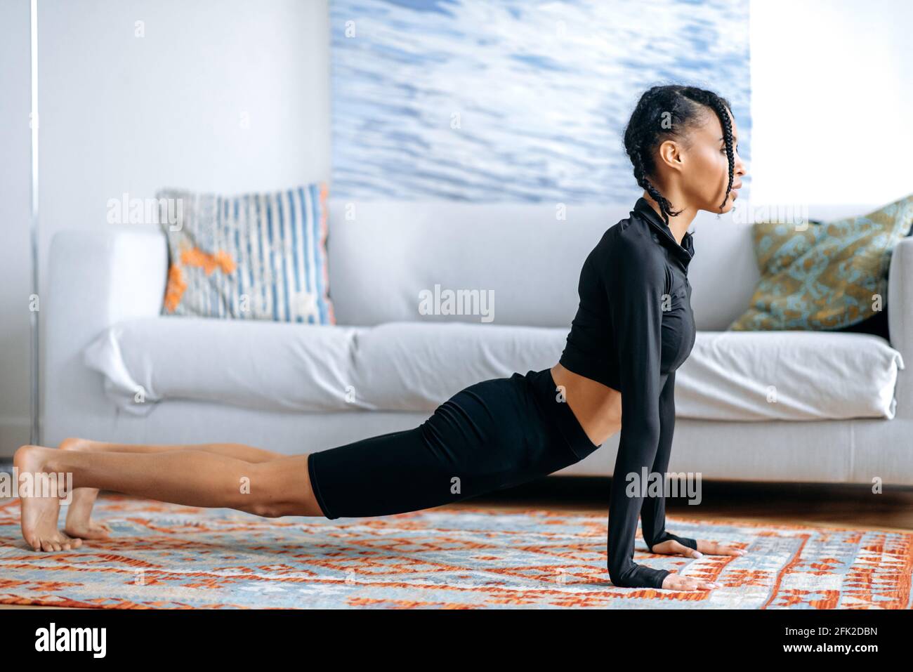 Attraente ragazza afroamericana sottile in nero sportswear, facendo stretching a casa sul pavimento, è impegnato fitness, conduce uno stile di vita sano, la cura per la salute Foto Stock