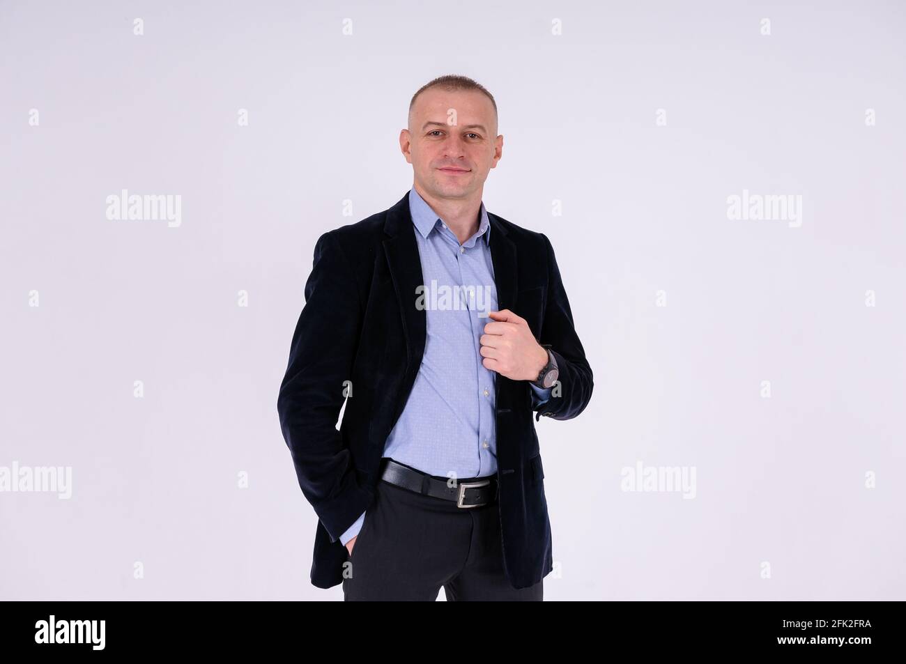 Uomo che indossa una camicia blu, pantaloni neri e una giacca blu su sfondo bianco Foto Stock
