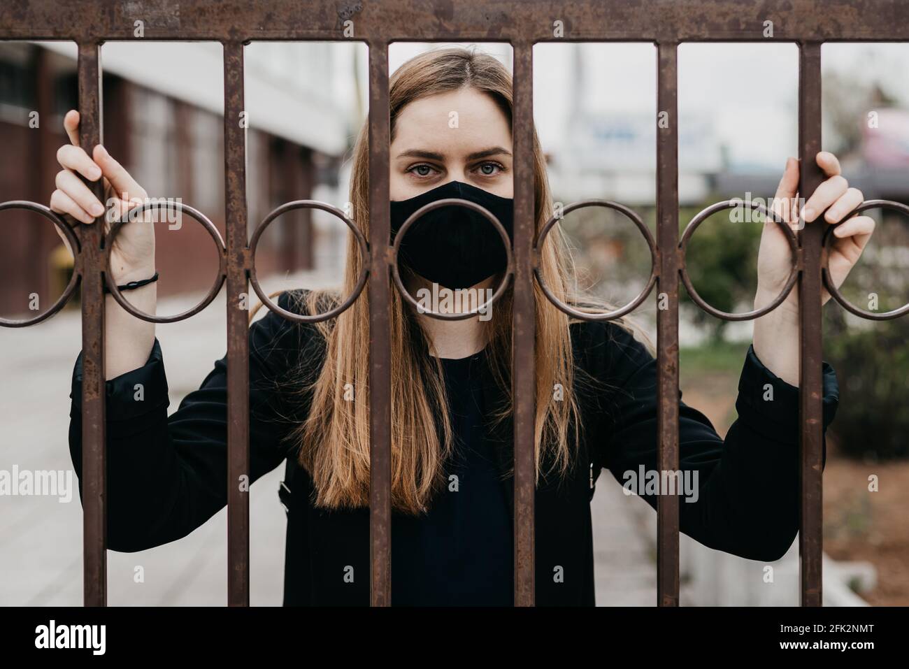 donna con maschera facciale dietro le sbarre all'aperto, concetto di blocco covid 19 Foto Stock