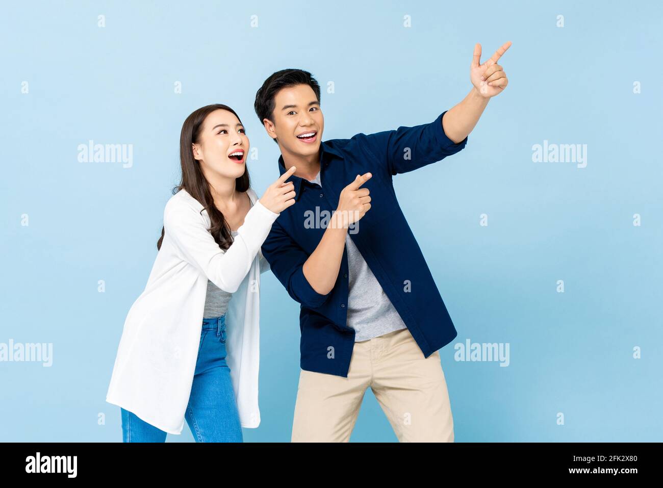 Sorridente coppia asiatica eccitata che punta le mani verso l'alto verso lo spazio vuoto su sfondo blu chiaro isolato Foto Stock
