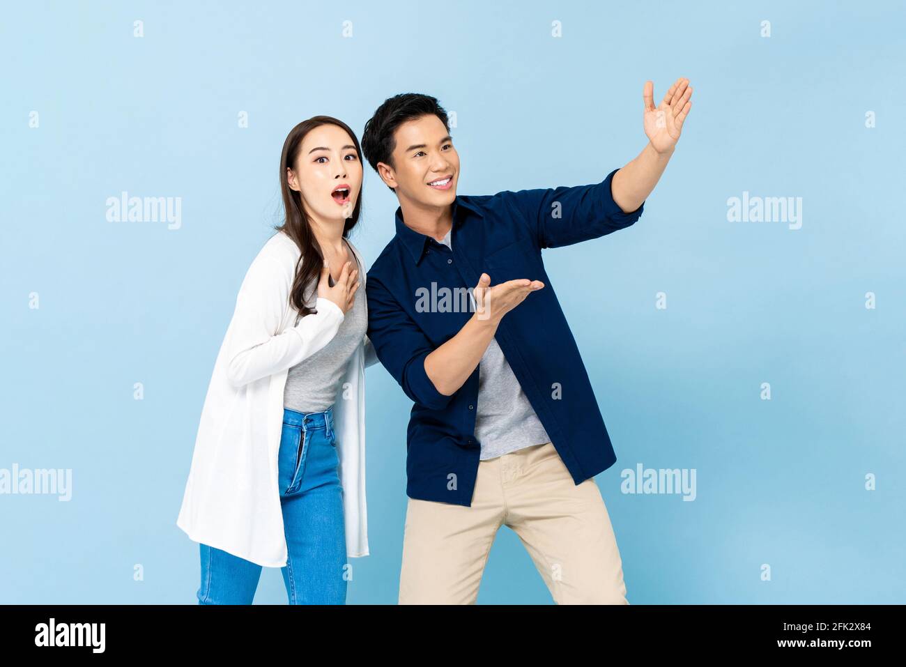 Scioccata coppia asiatica stupita che punta le mani fino a spazio vuoto sopra su sfondo blu chiaro isolato Foto Stock