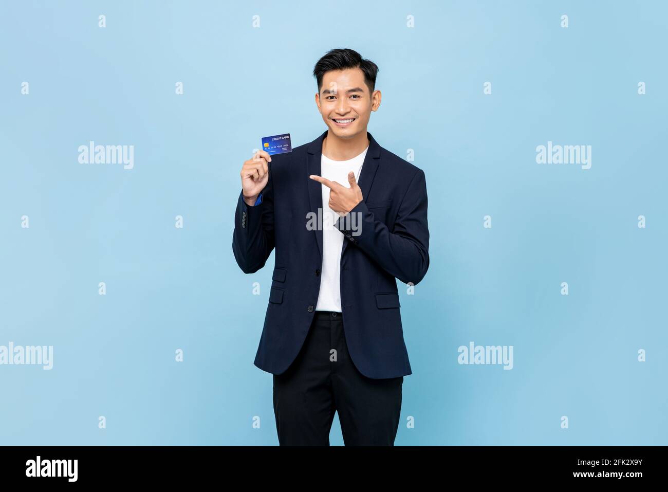 Bel bel bell'uomo del sud-est asiatico in tenuta blazer semi formale carta di credito su sfondo isolato blu chiaro dello studio Foto Stock