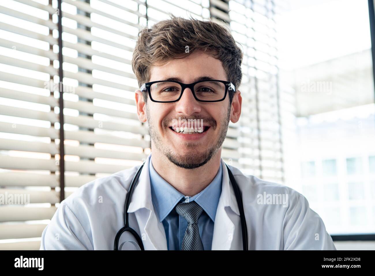 Felice giovane medico sorridente alla macchina fotografica mentre fa la videochiamata in linea, concetti di servizio di consulazione medica domestica Foto Stock