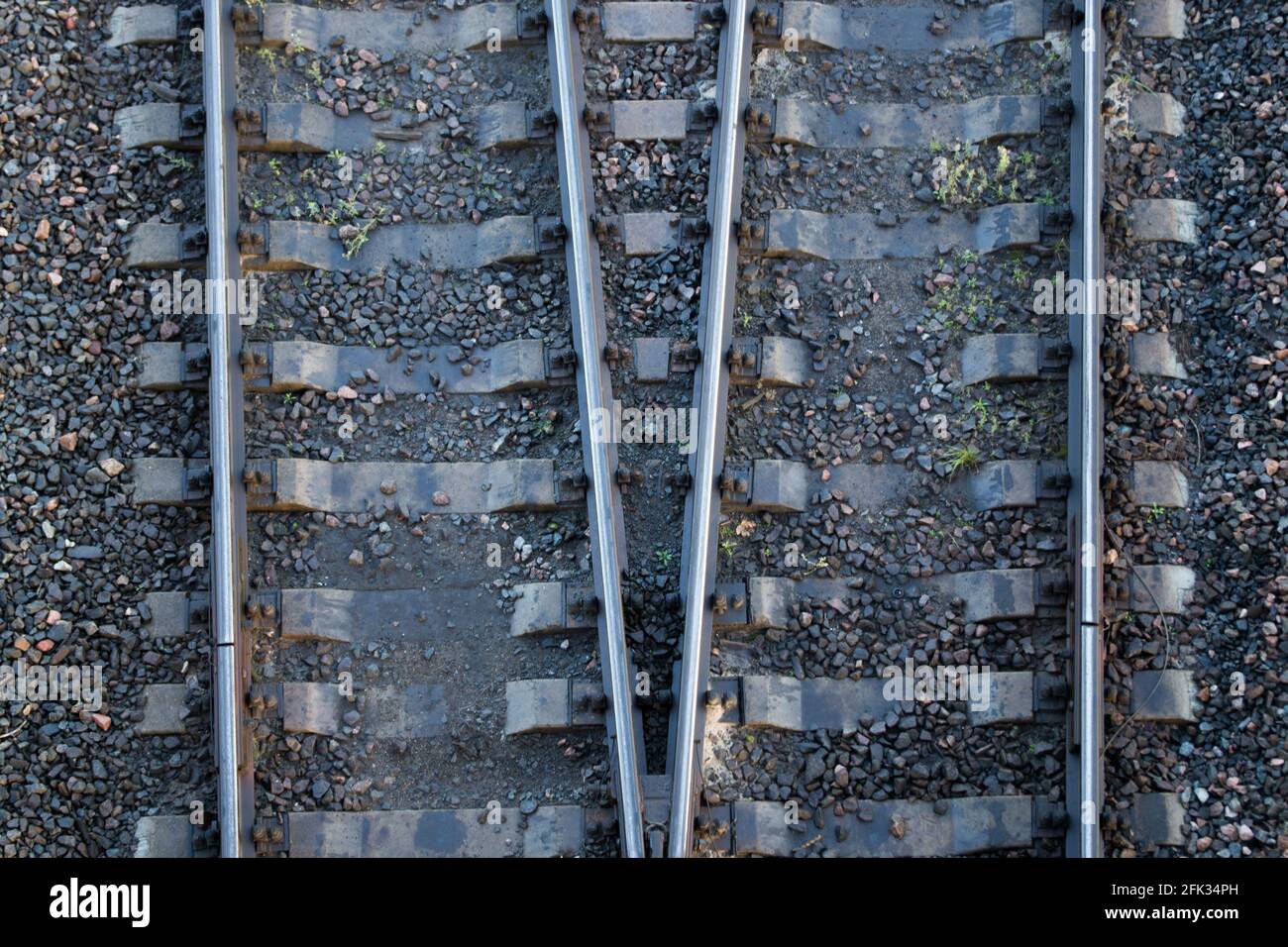 Due coppie di rotaie con traversine di binari ferroviari divergono in direzioni diverse, con tracce di grasso sullo sfondo di macerie. Concetto: Scegliere Foto Stock