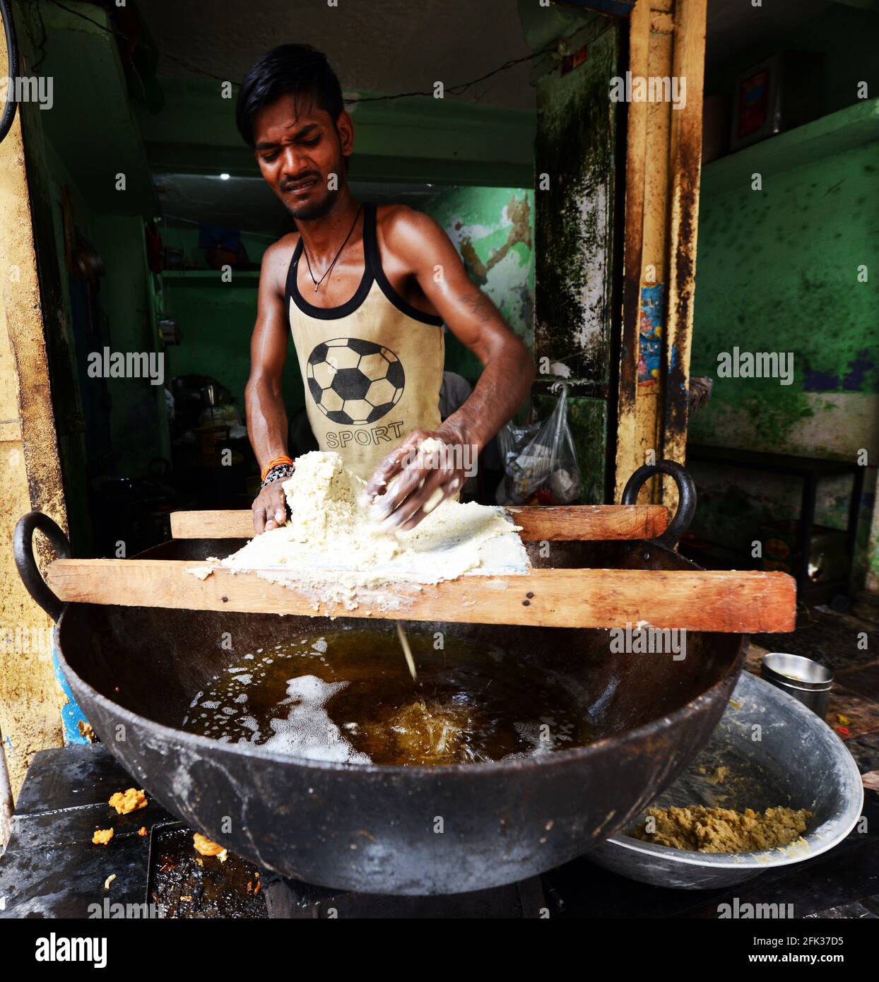 Un uomo indiano che prepara spuntini fritti in un piccolo negozio nella città vecchia di Varanasi, India. Foto Stock