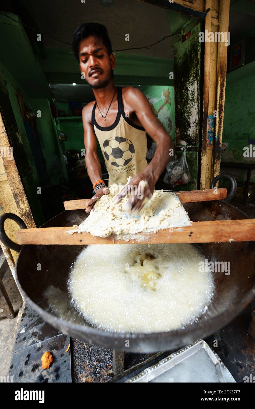 Un uomo indiano che prepara spuntini fritti in un piccolo negozio nella città vecchia di Varanasi, India. Foto Stock