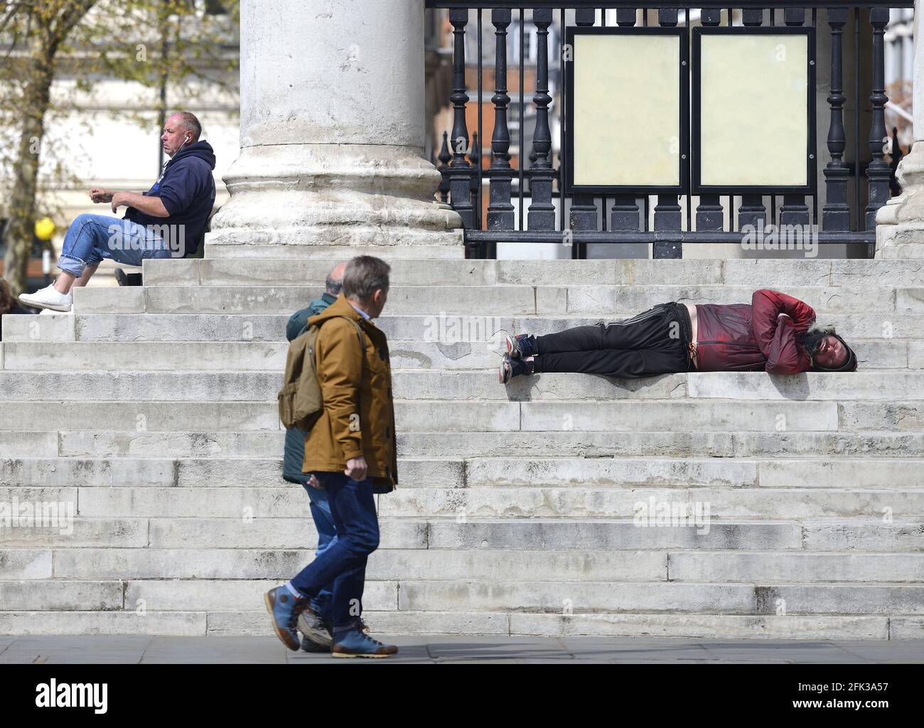 Londra, Inghilterra, Regno Unito. L'uomo addormentò sulle scale di San Martino nella Chiesa dei campi, Trafalgar Square - persone che camminano oltre Foto Stock