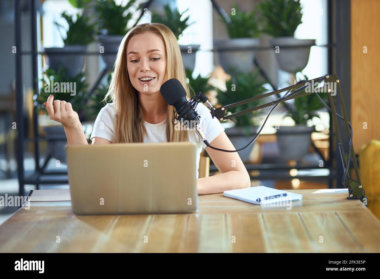 Vista frontale di una giovane donna attraente che racconta informazioni interessanti con il microfono moderno in trasmissione dal vivo. Concetto di comunicazione di processo con le persone online. Foto Stock
