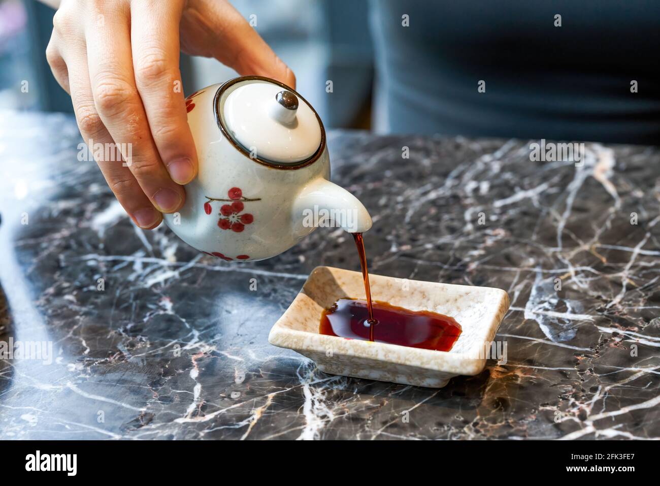 Una donna che mangia cibo giapponese sta versando salsa di soia Foto Stock
