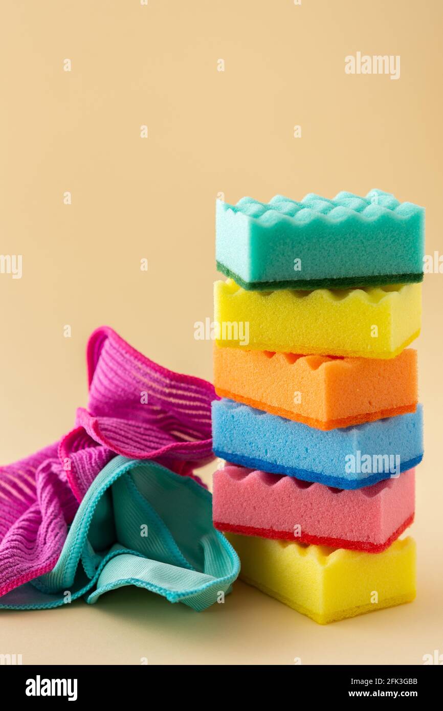 Pila di spugne per lavastoviglie multicolore e tovaglioli in microfibra su fondo beige neutro, cucina casalinghi e concetto di pulizia Foto Stock